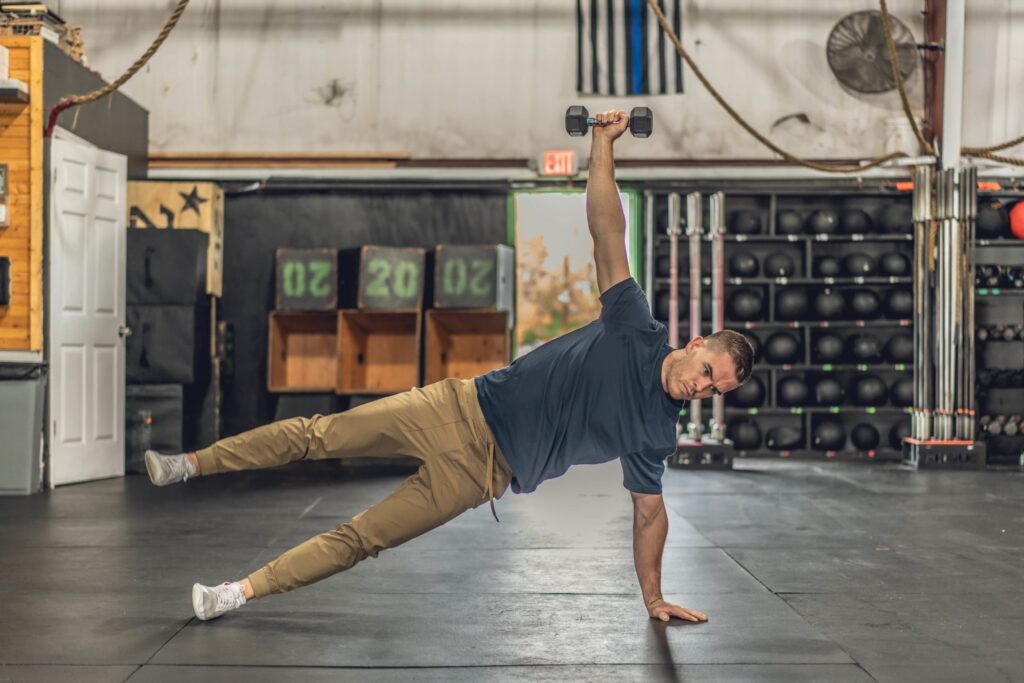 A member holding a side plank with a dumbbell overhead